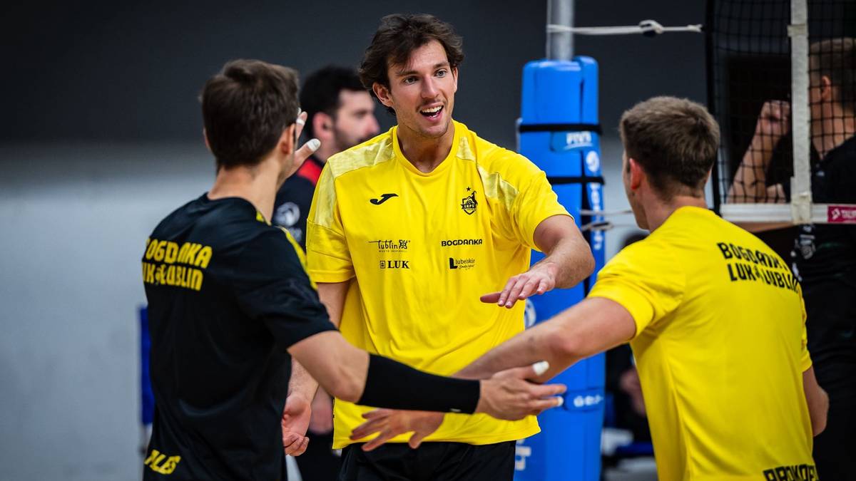 Trzech siatkarzy w żółtych koszulkach, dwóch z nich wita się z trzecim, który jest w środku. Wszyscy uśmiechnięci.