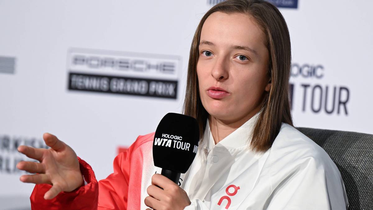 Iga Świątek, polska tenisistka, w białej koszuli i czerwonej kurtce, mówi do mikrofonu z logo WTA Tour.