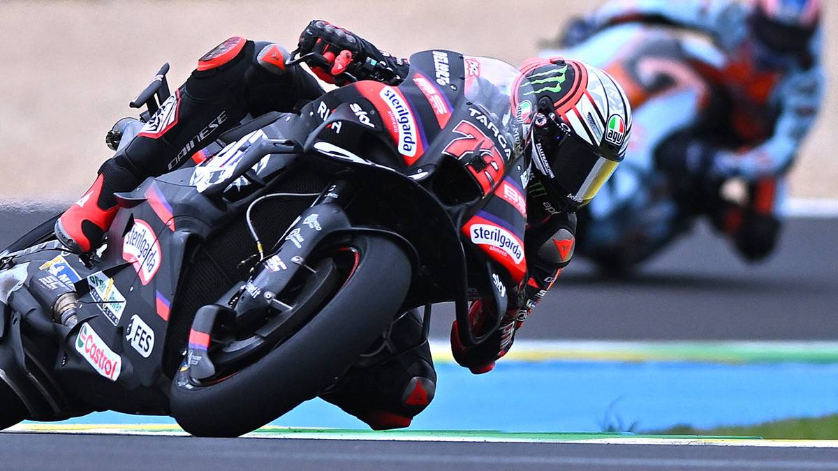 Dwóch motocyklistów ściga się na torze, jeden pochylony w zakręcie na pierwszym planie, drugi w tle.