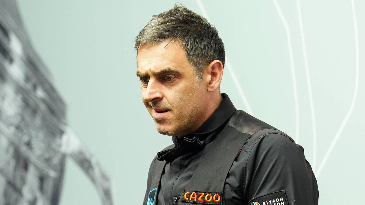 Ronnie O'Sullivan, sportowiec snookera, w czarnej koszulce z logo CAZOO, na jasnym tle.