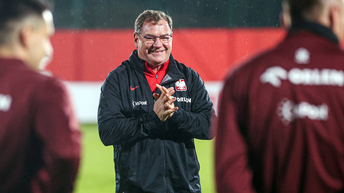 Trener Jan Urban uśmiecha się na tle piłkarzy reprezentacji Polski.