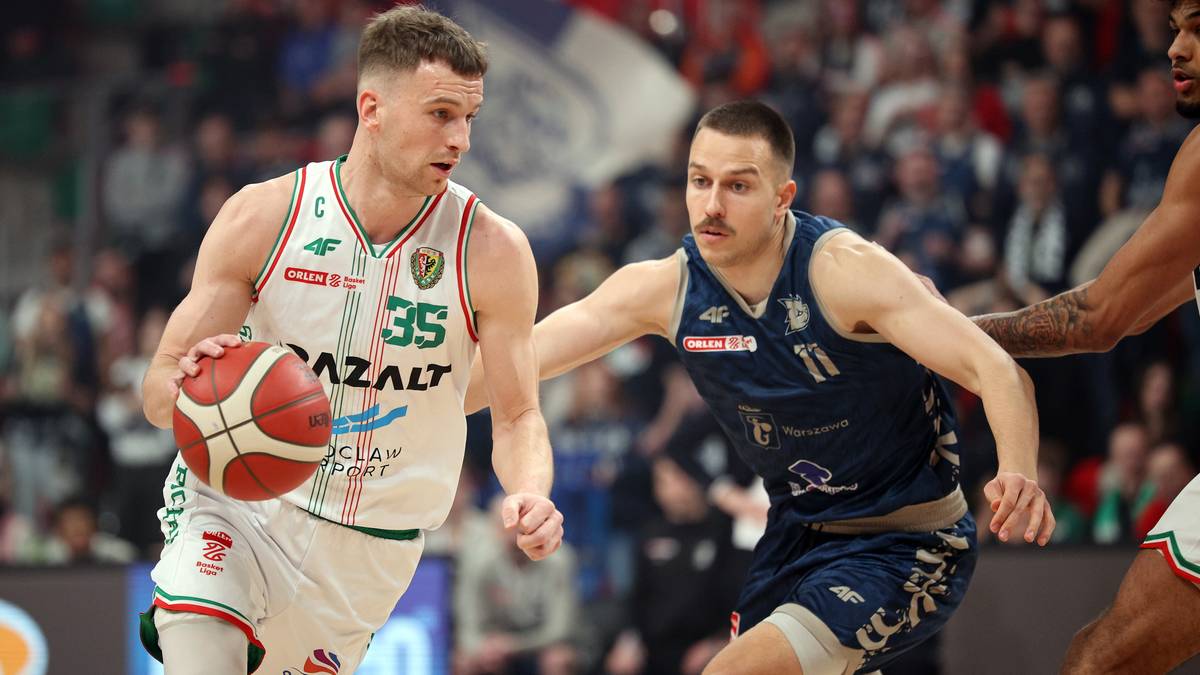 Koszykarz prowadzący piłkę podczas meczu, broniony przez przeciwnika.