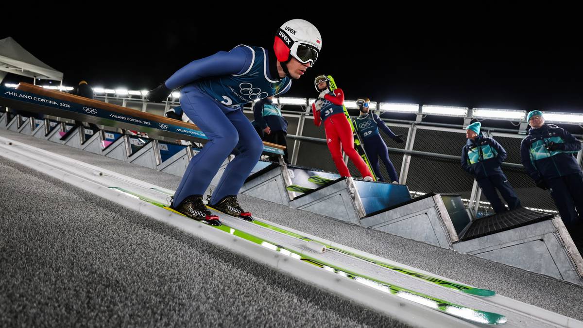 Skoczek narciarski w pozycji startowej na rozbiegu skoczni.