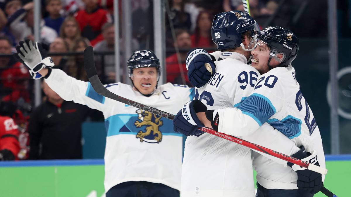 Trzech hokeist&oacute;w w białych strojach z niebieskimi detalami cieszy się z wygranej, przytulając się na lodowisku.