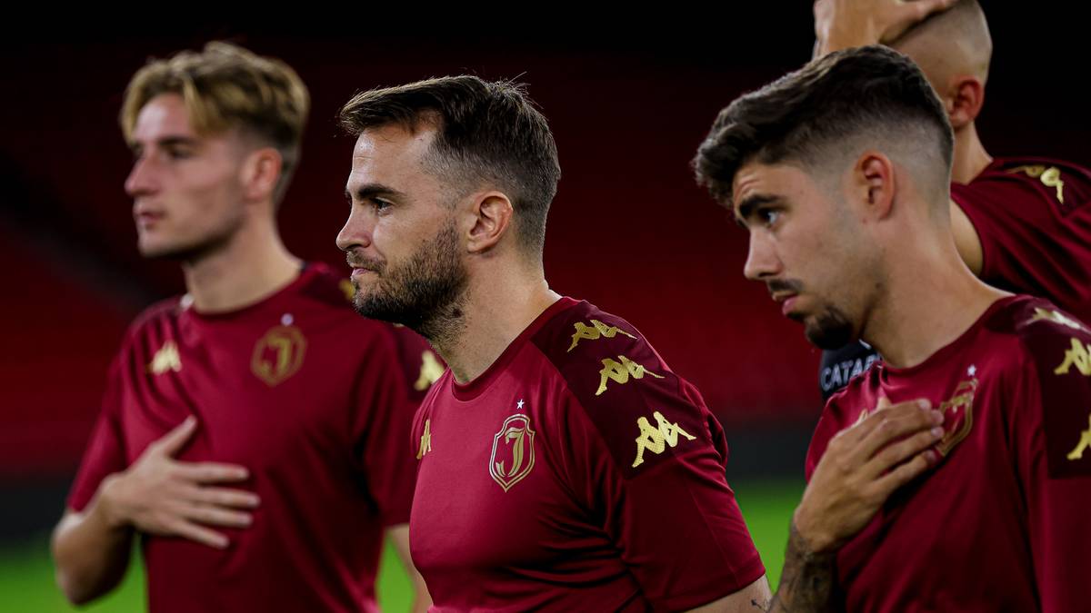 Trzech mężczyzn w bordowych koszulkach piłkarskich z wyszytym herbem klubu, ustawionych obok siebie.