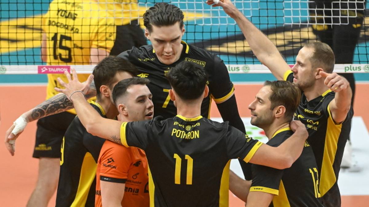 Grupa siatkarzy w czarnych koszulkach z żółtymi detalami cieszy się po wygranym meczu.