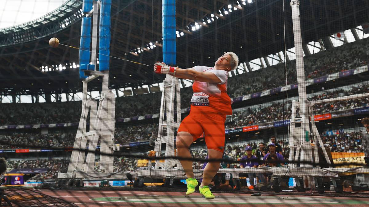 Zawodnik rzuca młotem podczas zawodów lekkoatletycznych, w tle trybuny stadionu.