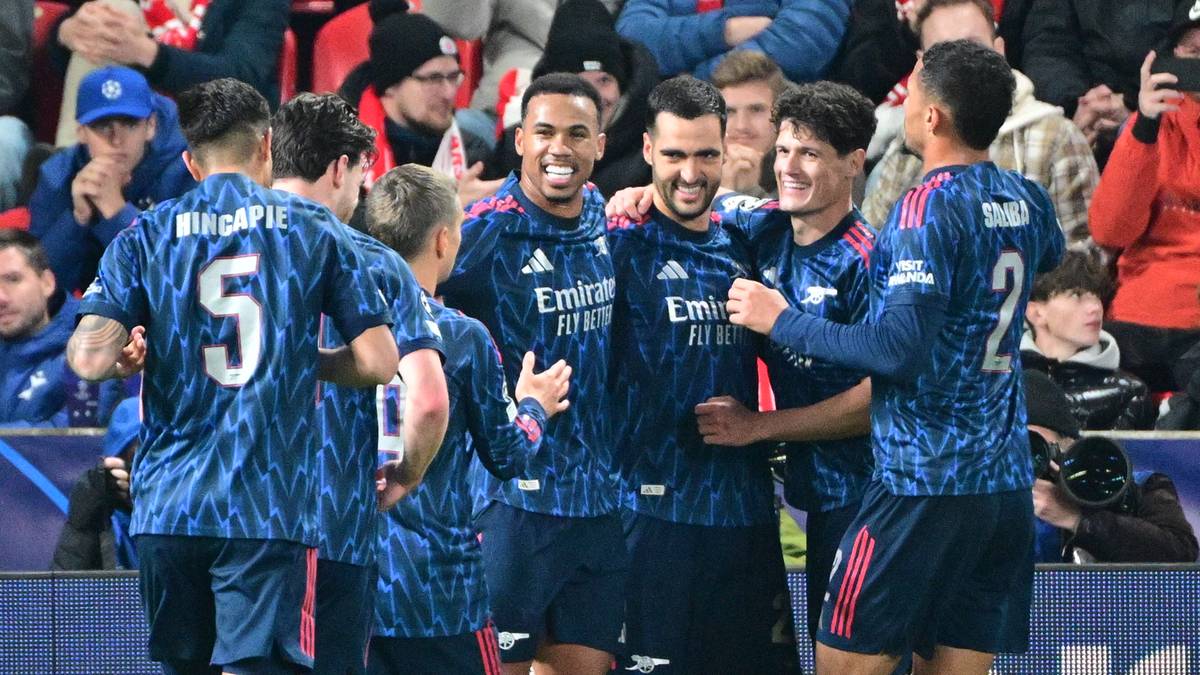 Piłkarze Arsenalu Londyn w niebieskich strojach z białymi akcentami świętują radośnie na boisku, przytulając się nawzajem.