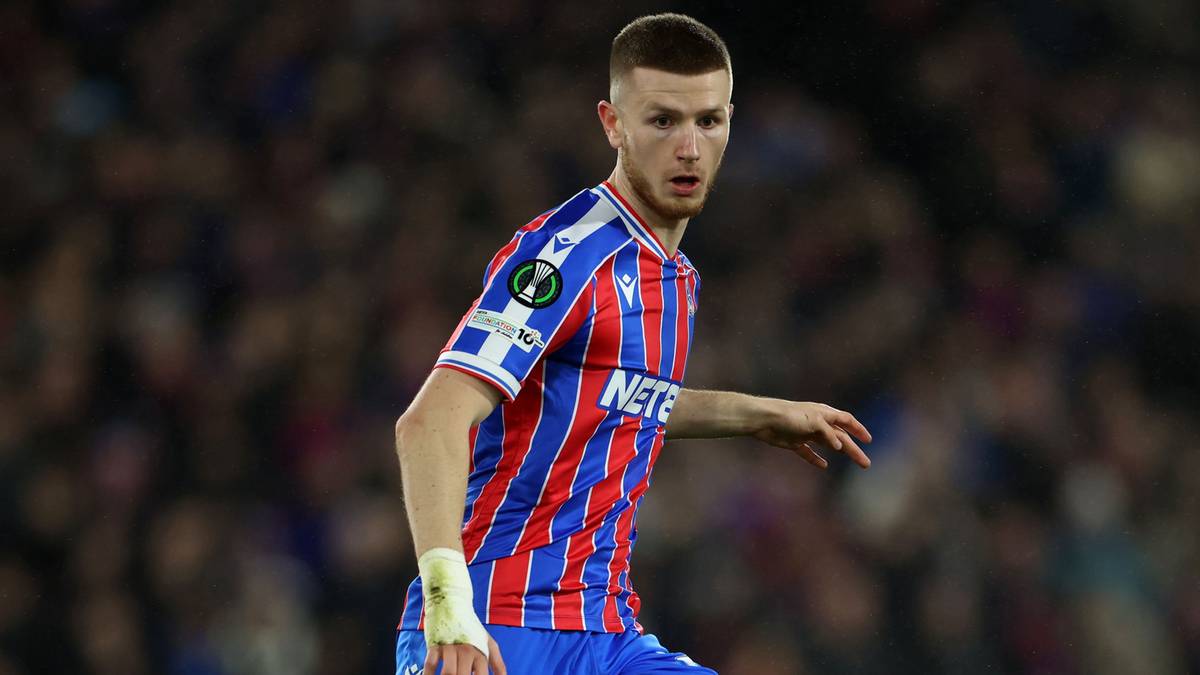 Piłkarz w pasiastej koszulce prowadzi piłkę na boisku.