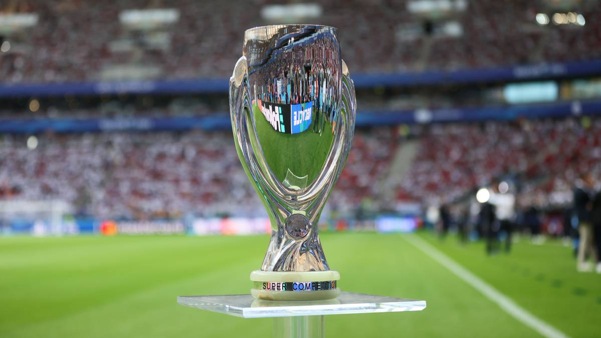 Trofeum Superpucharu UEFA na tle stadionu piłkarskiego z widzami na trybunach.