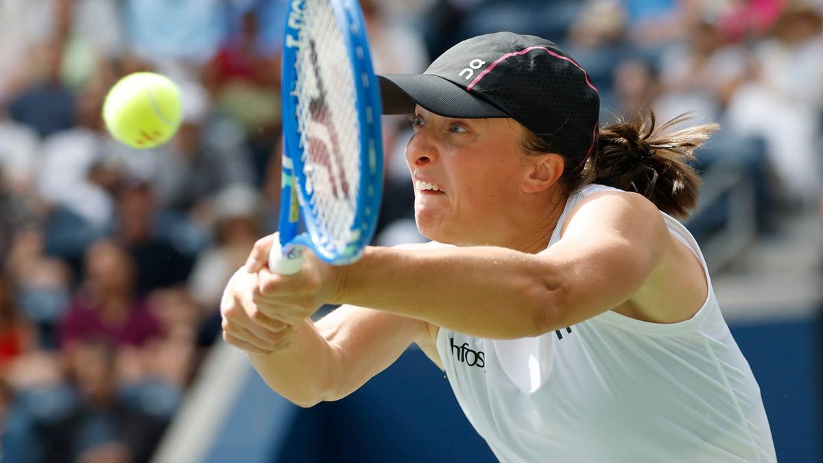 Profesjonalna tenisistka Iga Świątek w trakcie meczu, skupiona na odbiciu piłki rakietą. Koncentracja na jej twarzy jest wyraźna.