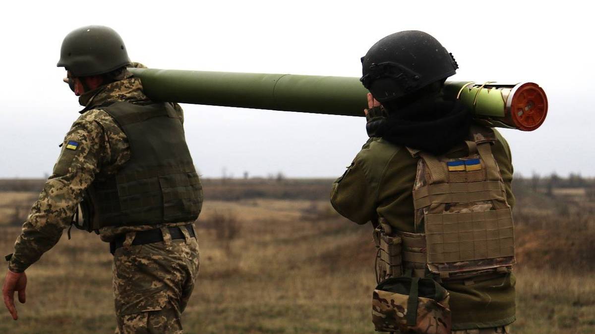 Dwóch żołnierzy w mundurach taktycznych i hełmach niesie na ramieniu długi, zielony pocisk.