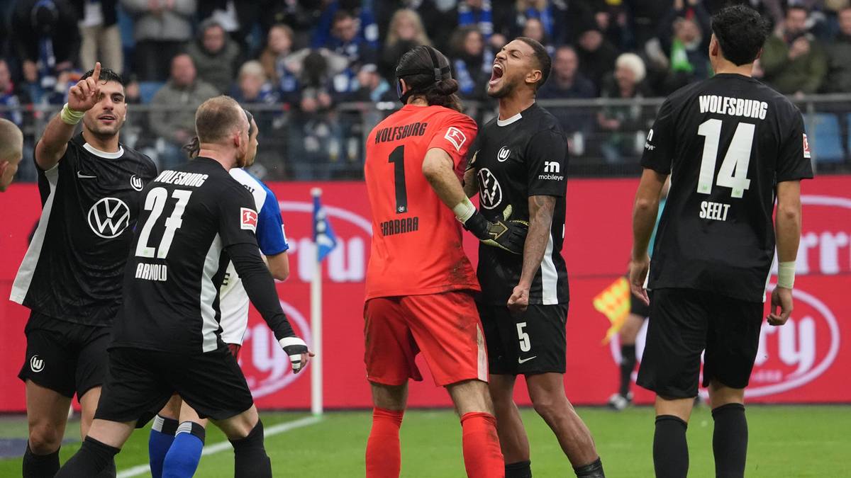 Piłkarze FC Augsburg świętują zdobycie bramki, wśród nich bramkarz Rafał Gikiewicz. Zawodnicy w czarnych strojach cieszą się z sukcesu na boisku, a na trybunach widać kibiców.