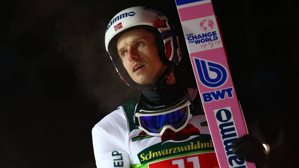 Portret skoczka narciarskiego w kasku i goglach, trzymającego nartę z logo "Change the World"