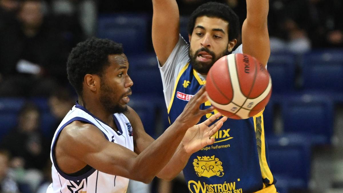 Koszykarz w białej koszulce próbuje odebrać piłkę koszykarzowi w niebiesko-żółtej koszulce.