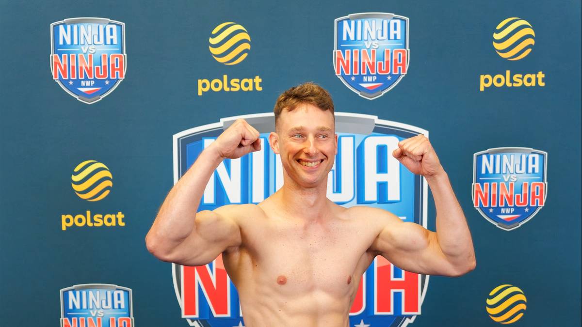 Jan Tatarowicz uśmiecha się, napinając bicepsy, na tle logo Ninja Warrior.