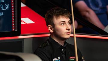 Antoni Kowalski, młody polski snookerzysta, wpatrzony przed siebie z kijem snookerowym.