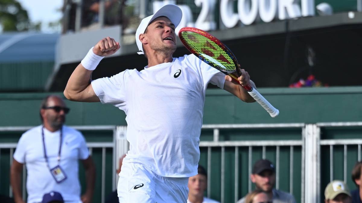 Tenisista w białej koszulce i spodenkach świętuje zdobyty punkt, unosząc rękę z rakietą tenisową do góry.