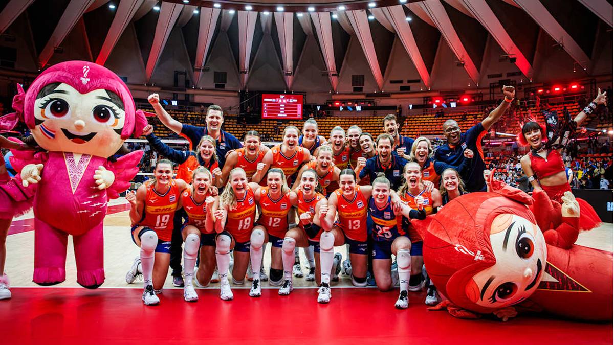 Druzyna siatkarek z siedmioma zawodniczkami, maszkotkami i trenerami pozująca do zdjecia po zwyciestwie w meczu.