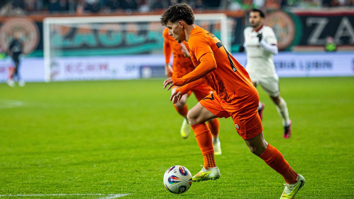 Piłkarz w pomarańczowym stroju prowadzi piłkę.