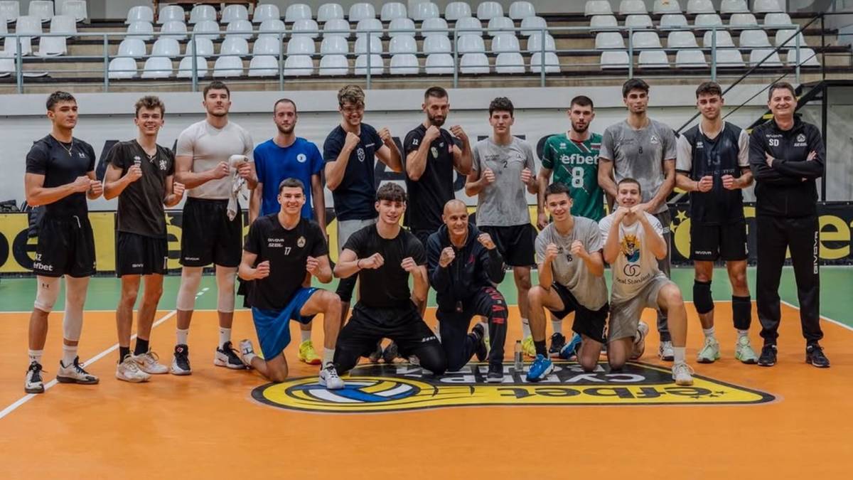 Grupa siatkarzy i trenerów sztuk walki pozuje do zdjęcia w hali sportowej.