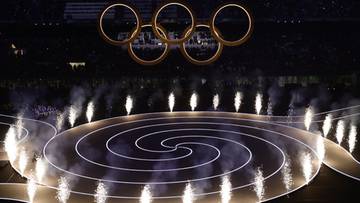 Widok na stadion podczas ceremonii otwarcia zimowych igrzysk olimpijskich, z widocznymi k&oacute;łkami olimpijskimi i efektami świetlnymi.