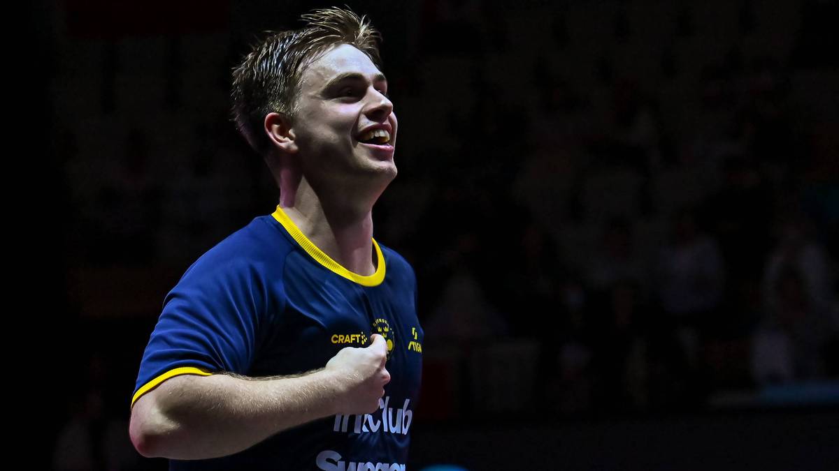 Mężczyzna w niebiesko-żółtej koszulce sportowej z napisem "Swegen Ahlsell", uśmiecha się z podniesioną głową i ręką na piersi.