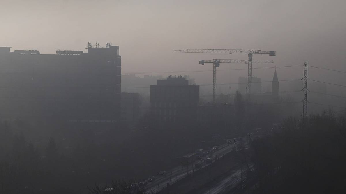 Widok na miasto w gęstej mgle z widocznymi budynkami i dźwigami budowlanymi.