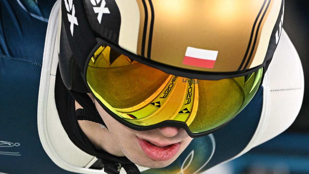 Zbliżenie na kask skoczka narciarskiego z widoczną polską flagą na wizjerze.