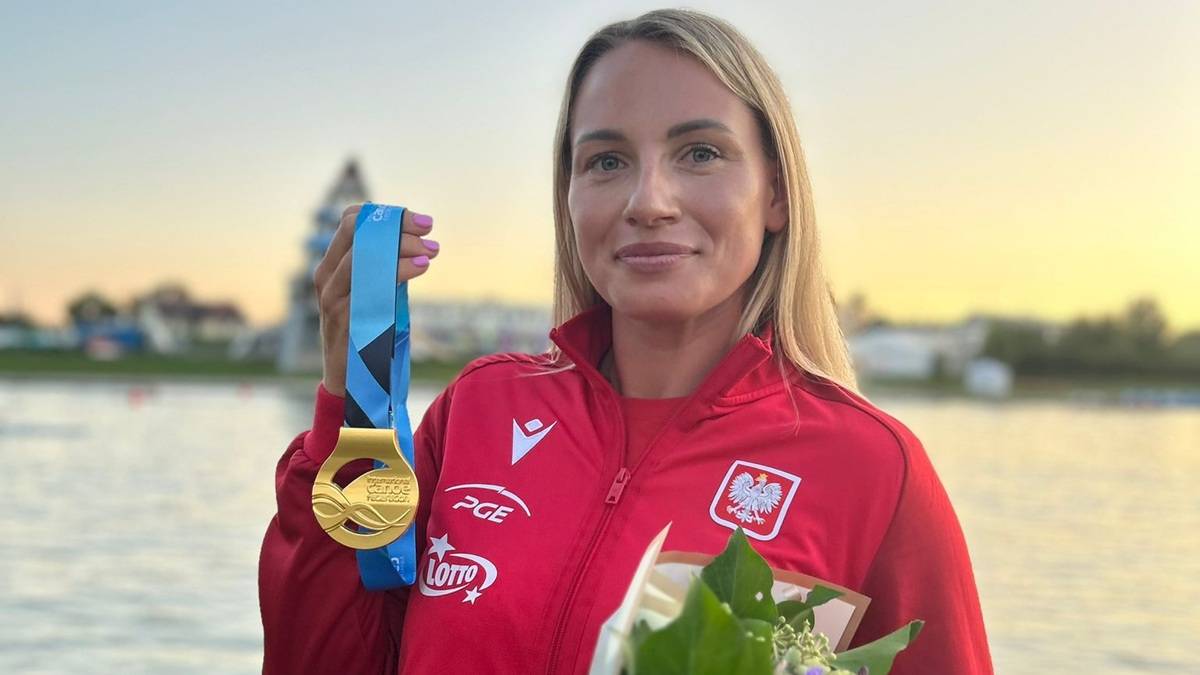 Kobieta w czerwonej kurtce sportowej z godłem Polski prezentuje złoty medal na niebieskiej wstążce.