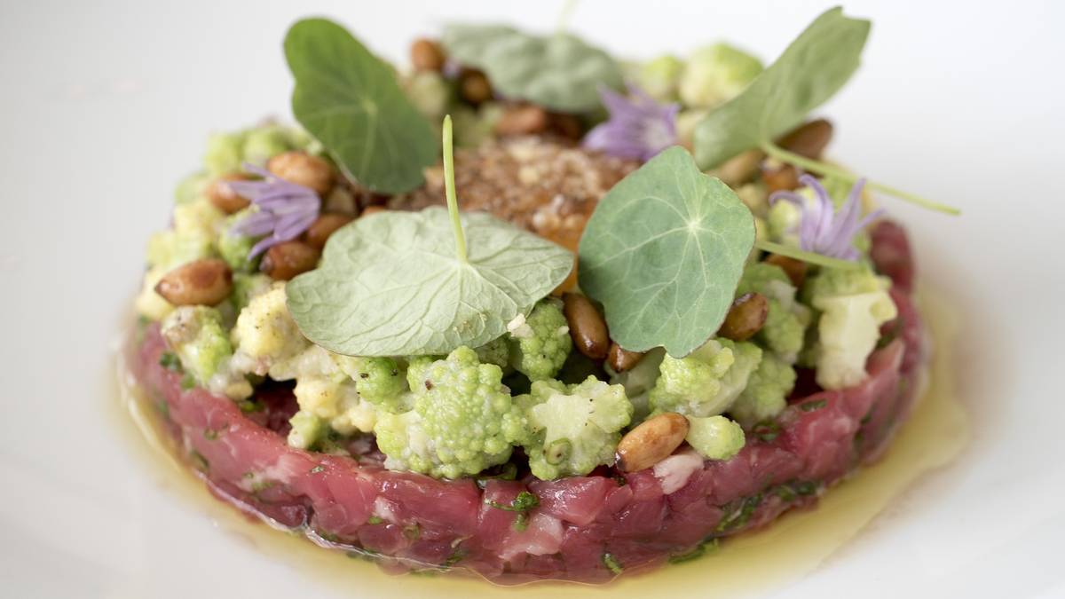 Wykwintnie podany tatar wołowy na talerzu, ozdobiony warzywami i ziołami.