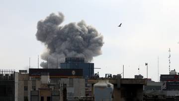 Duży słup dymu unoszący się nad zabudowaniami miejskimi.