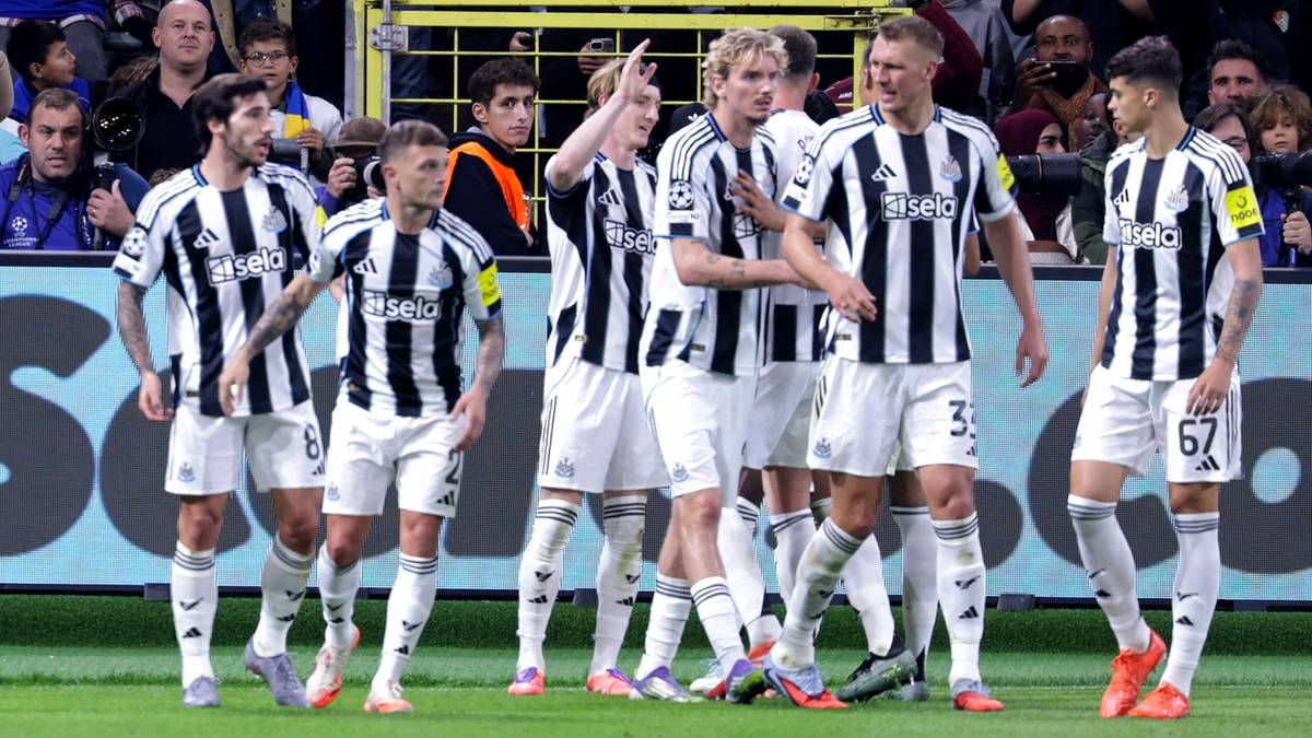 Grupa piłkarzy w białych strojach z czarnymi pasami, stojących na boisku piłkarskim, prezentujący emocje po meczu.