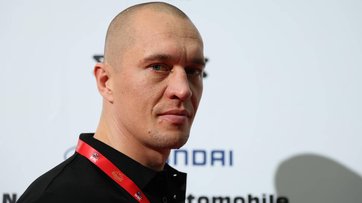 Portret mężczyzny z ogoloną głową, patrzącego w stronę obiektywu. Na szyi widoczny czerwony identyfikator. W tle logo Hyundai.