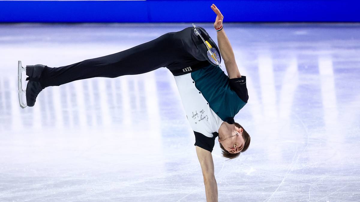 Łyżwiarz figurowy wykonuje figurę na lodzie, podpierając się jedną ręką.