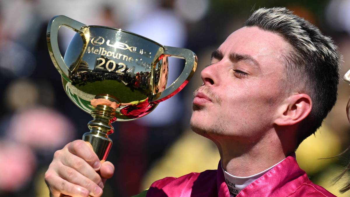 Młody mężczyzna w różowym stroju dżokeja całuje złoty puchar Melbourne Cup.