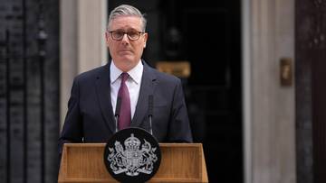 Keir Starmer przemawiający za m&oacute;wnicą przed budynkiem Downing Street 10, z herbem Wielkiej Brytanii na m&oacute;wnicy.