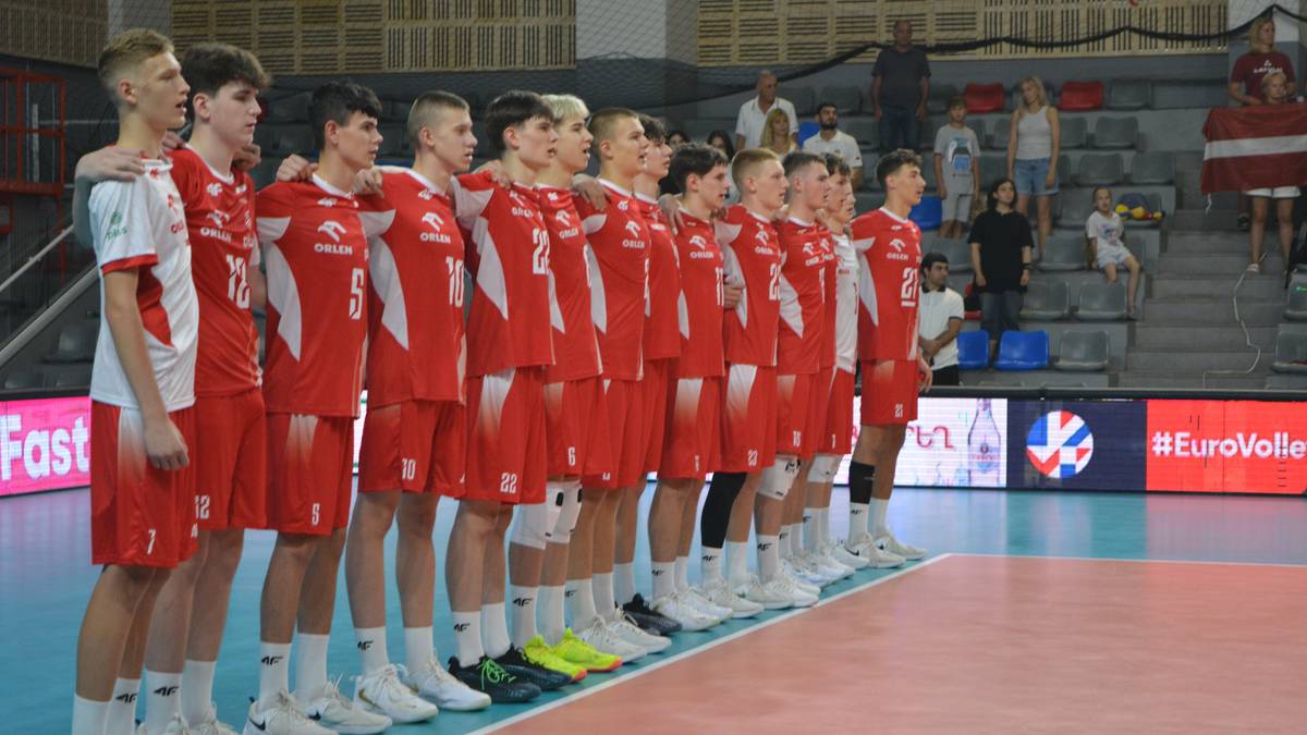 Reprezentacja Polski w siatkówce mężczyzn w czerwonych koszulkach i białych spodenkach stoi w rzędzie, patrząc przed siebie.