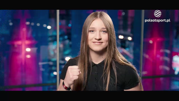 Julia Szeremeta, młoda kobieta z długimi włosami, w czarnej koszuli, unosi zaciśniętą w pięść prawą rękę.