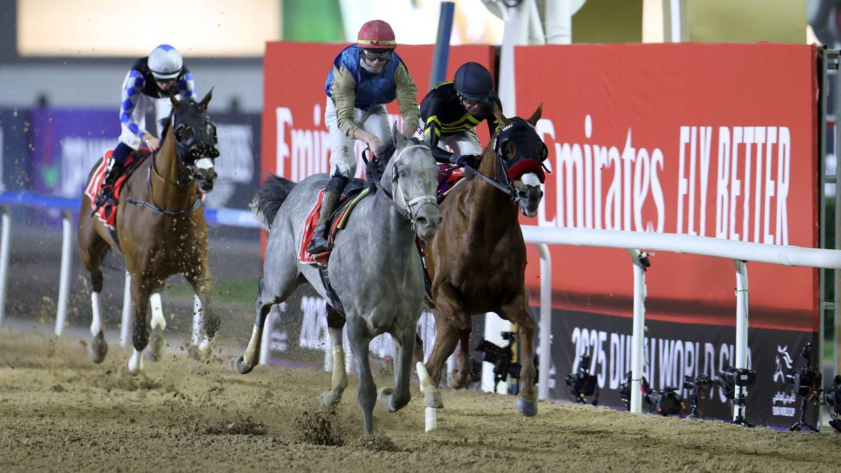 Trzech dżokej&oacute;w na koniach ścigających się na torze wyścigowym z widocznym w tle banerem Emirates