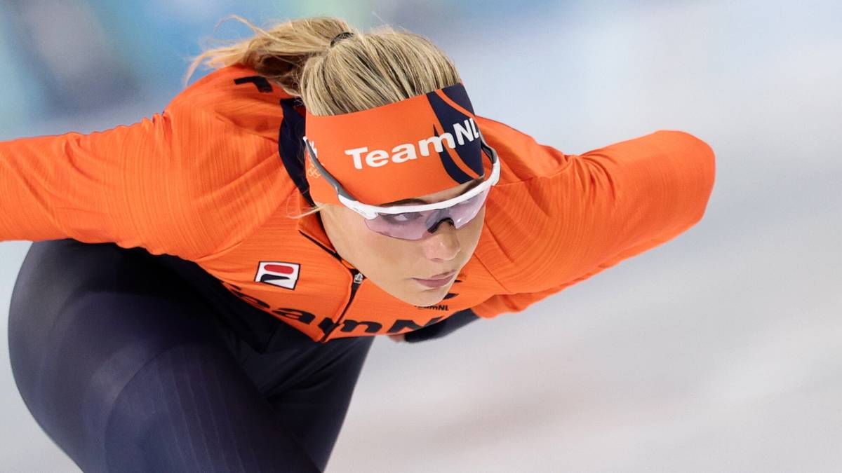 Zawodniczka w pomarańczowym stroju z opaską na głowie z napisem "TeamNL" jedzie na łyżwach