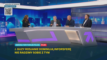 Czterech uczestnik&oacute;w debaty telewizyjnej w nowoczesnym studiu siedzi przy dużym, p&oacute;łokrągłym stole na tle niebieskich ekran&oacute;w.