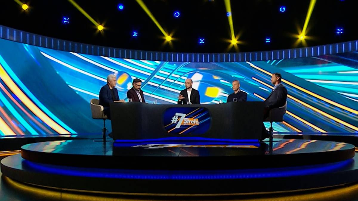 W studiu telewizyjnym panel dyskusyjny z udziałem pięciu osób. W tle ekrany z dynamicznymi wzorami i oświetleniem. W dolnym prawym rogu znajduje się osoba wykonująca gesty języka migowego.