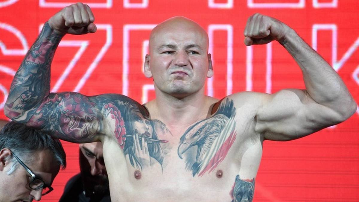 Mężczyzna z ogoloną głową i tatuażami na ramionach i klatce piersiowej napina bicepsy.