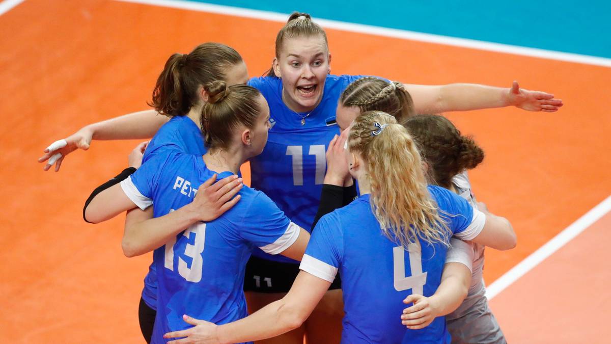Grupa siatkarek w niebieskich strojach cieszy się ze zwycięstwa, przytulając się do siebie na boisku.