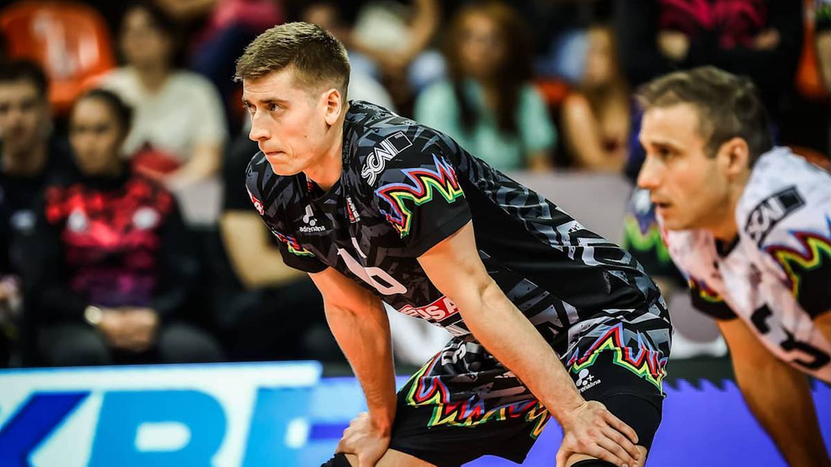 Dw&oacute;ch siatkarzy w strojach sportowych na boisku siatkarskim.