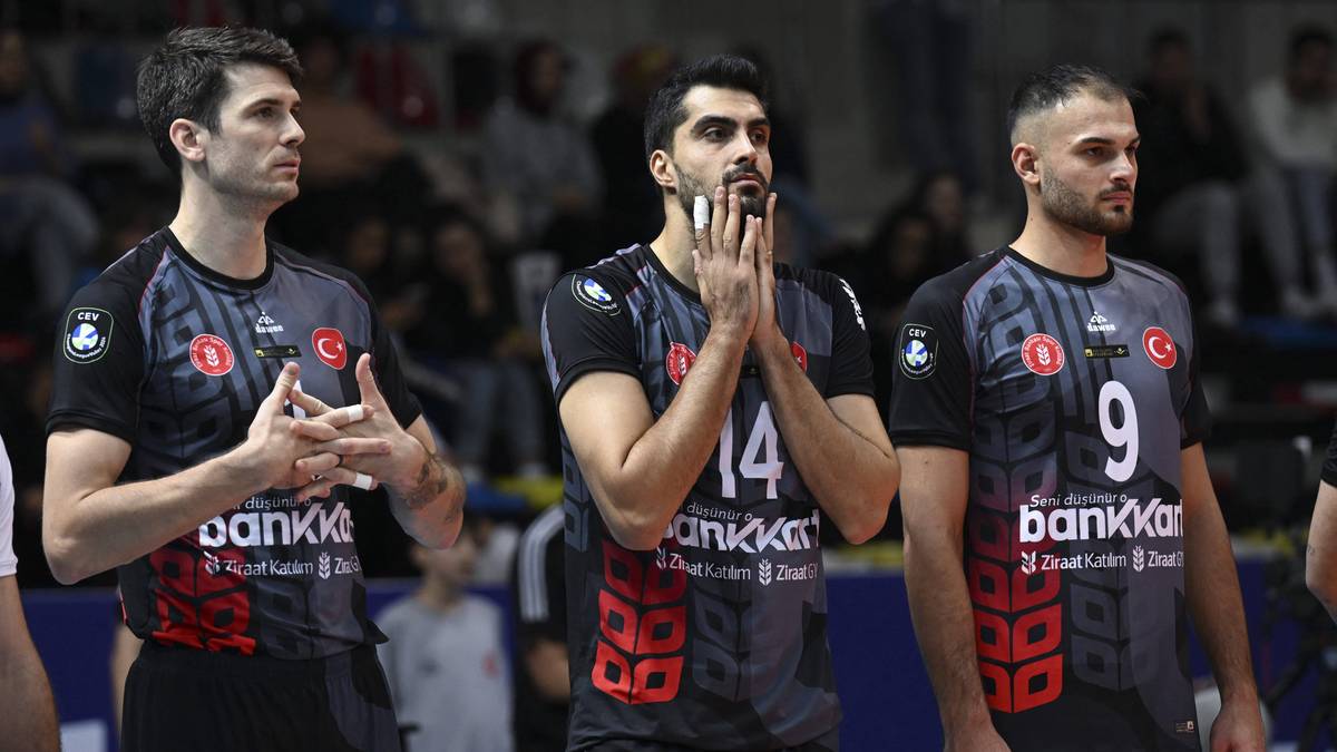 Trzech siatkarzy w czarnych koszulkach z czerwonymi akcentami, jeden z nich trzyma dłonie przy twarzy, wyrażając niepokój.