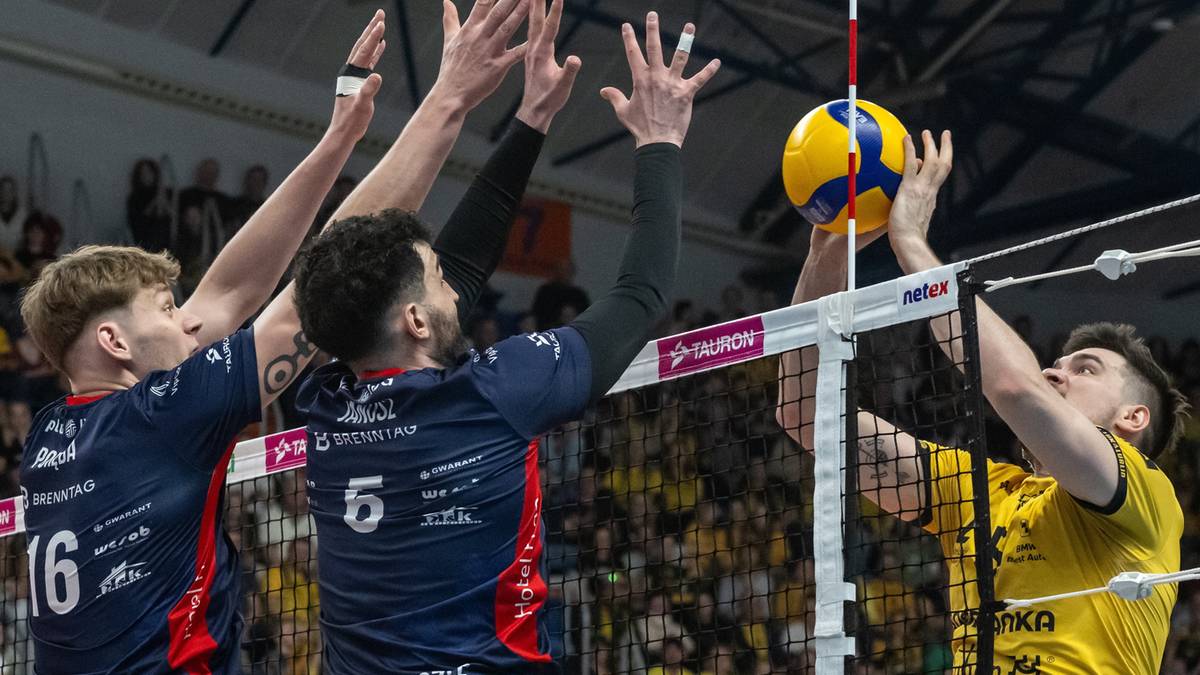 Siatkarze w akcji podczas meczu, jeden z nich serwuje piłkę nad siatką.