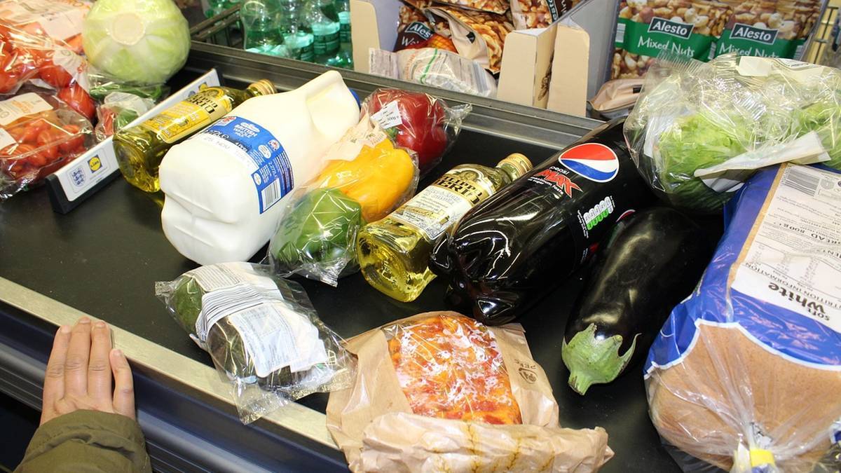 Produkty spożywcze na taśmie sklepowej, w tym warzywa, mleko i napoje.