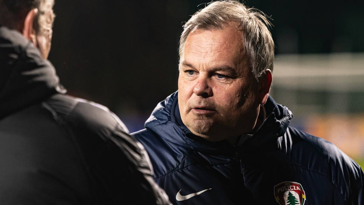 Mężczyzna w niebieskiej kurtce z zapiętym kołnierzem, patrzy w bok z poważną miną.